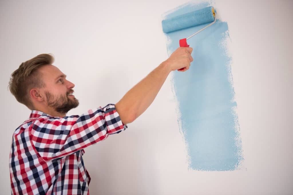 Pape peignant un mur en bleu avec une peinture écologique